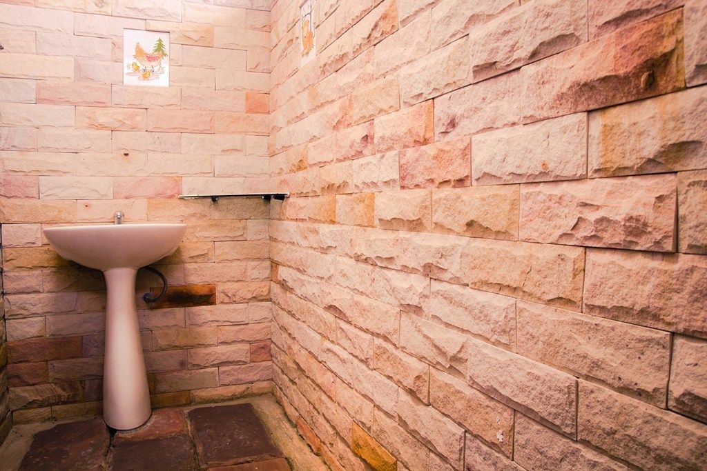 Un baño con un lavamanos blanco frente a una pared de piedra, un estante pequeño y un cuadro enmarcado.