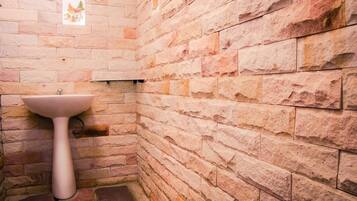 Un baño con un lavamanos blanco frente a una pared de piedra, un estante pequeño y un cuadro enmarcado.