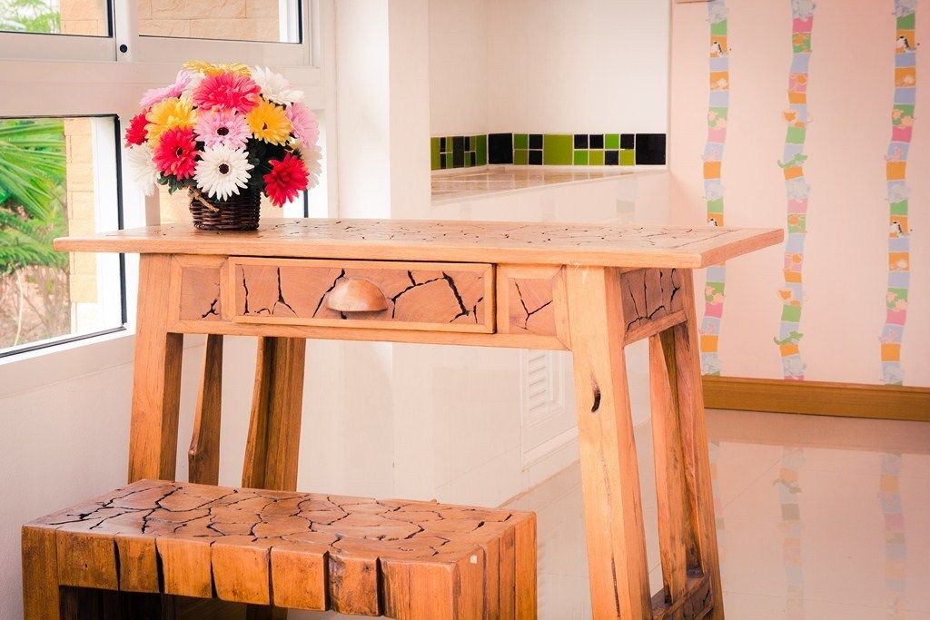 Una mesa de madera con un banco, un jarrón de flores y una pared colorida con personajes de caricatura.
