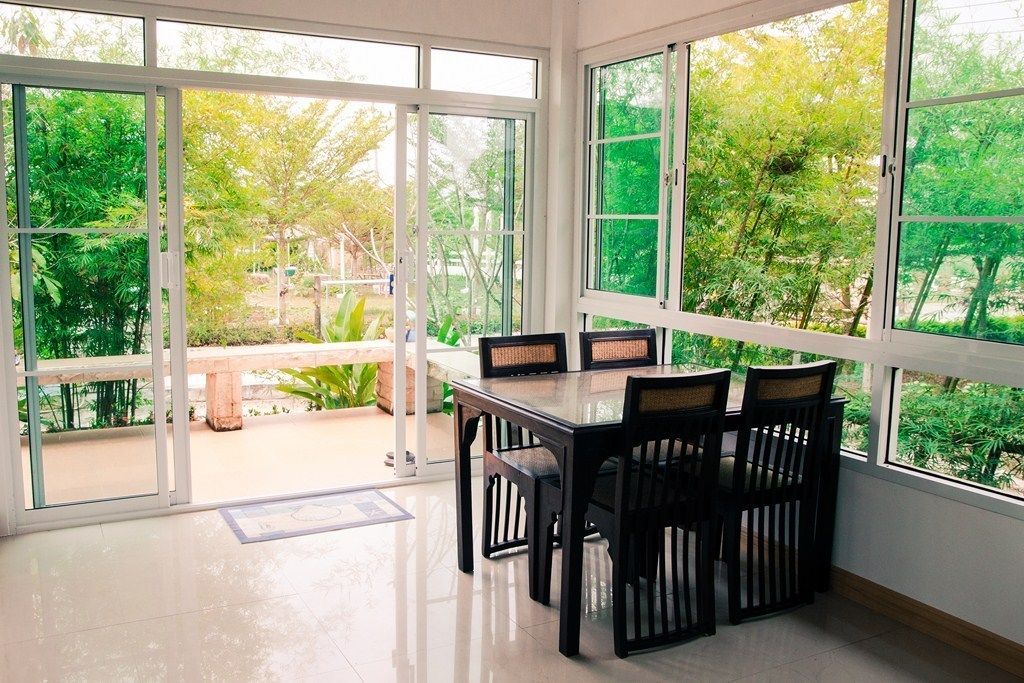 Un espace repas avec une table et des chaises en verre, de grandes fenêtres offrant une vue sur la verdure environnante.