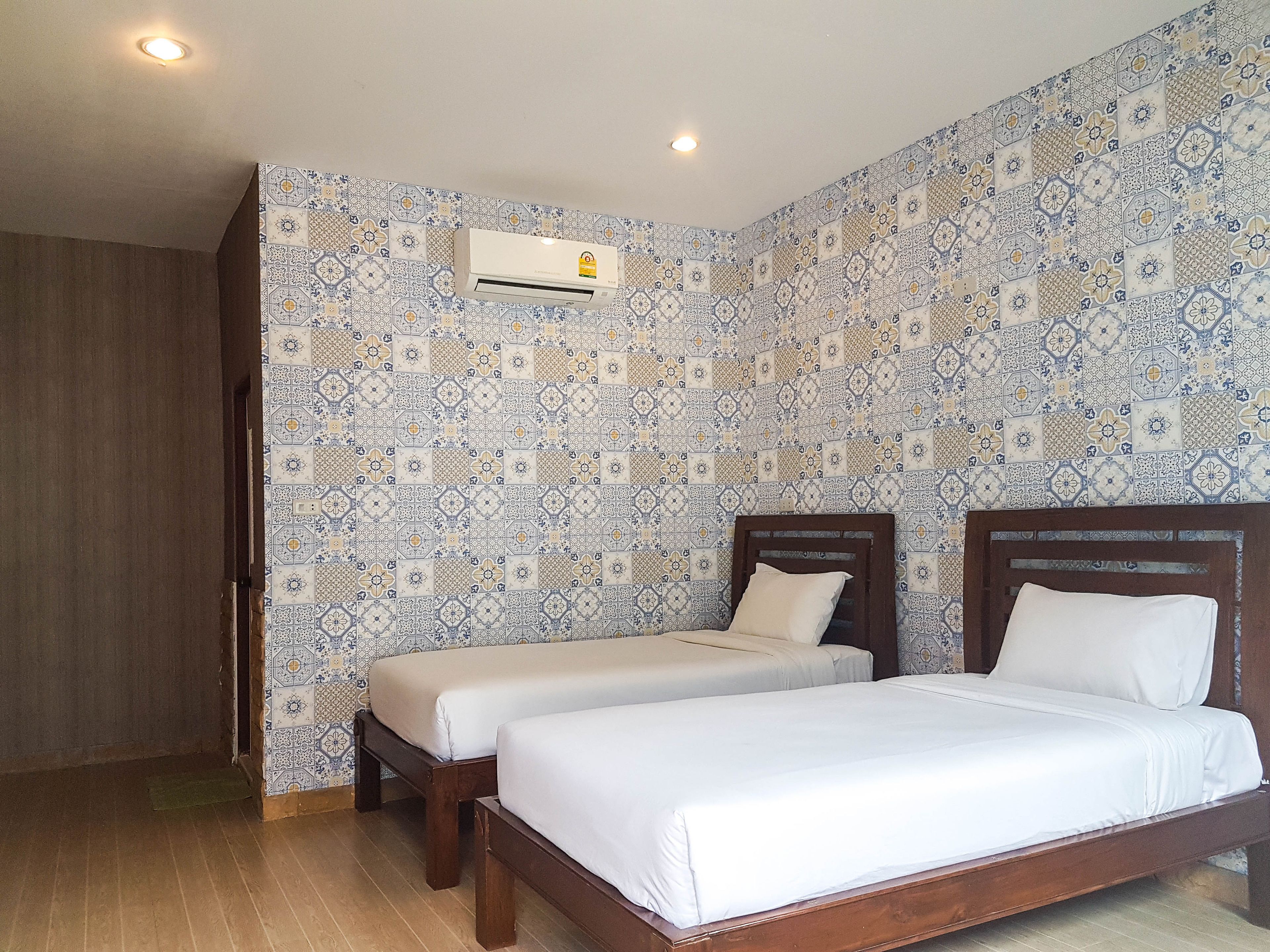 A bedroom with two beds, a wooden floor, patterned wallpaper, and an air conditioning unit.