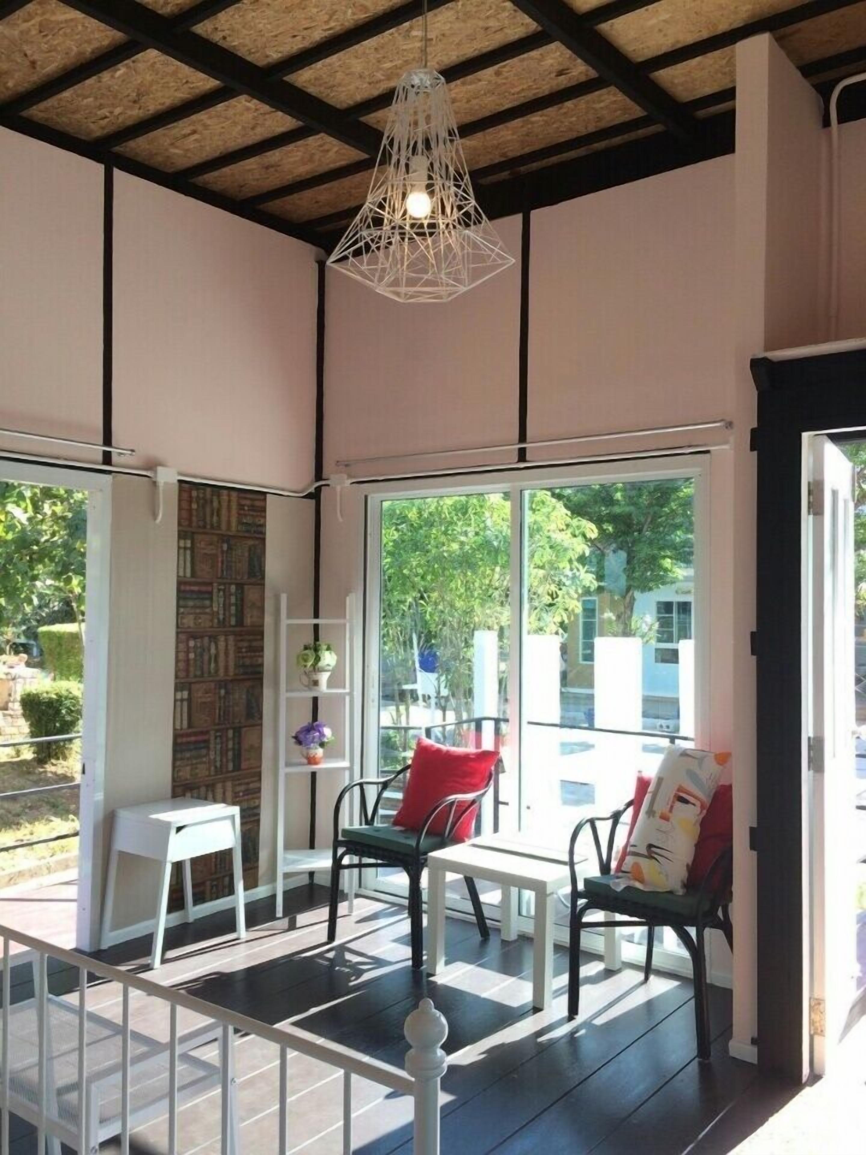 An indoor seating area with a wooden ceiling, a hanging light fixture, and a view of greenery outside.