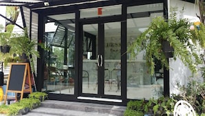 Een modern gebouw met grote glazen deuren, een zwart frame en een klein terras met een houten tafel en stoelen.