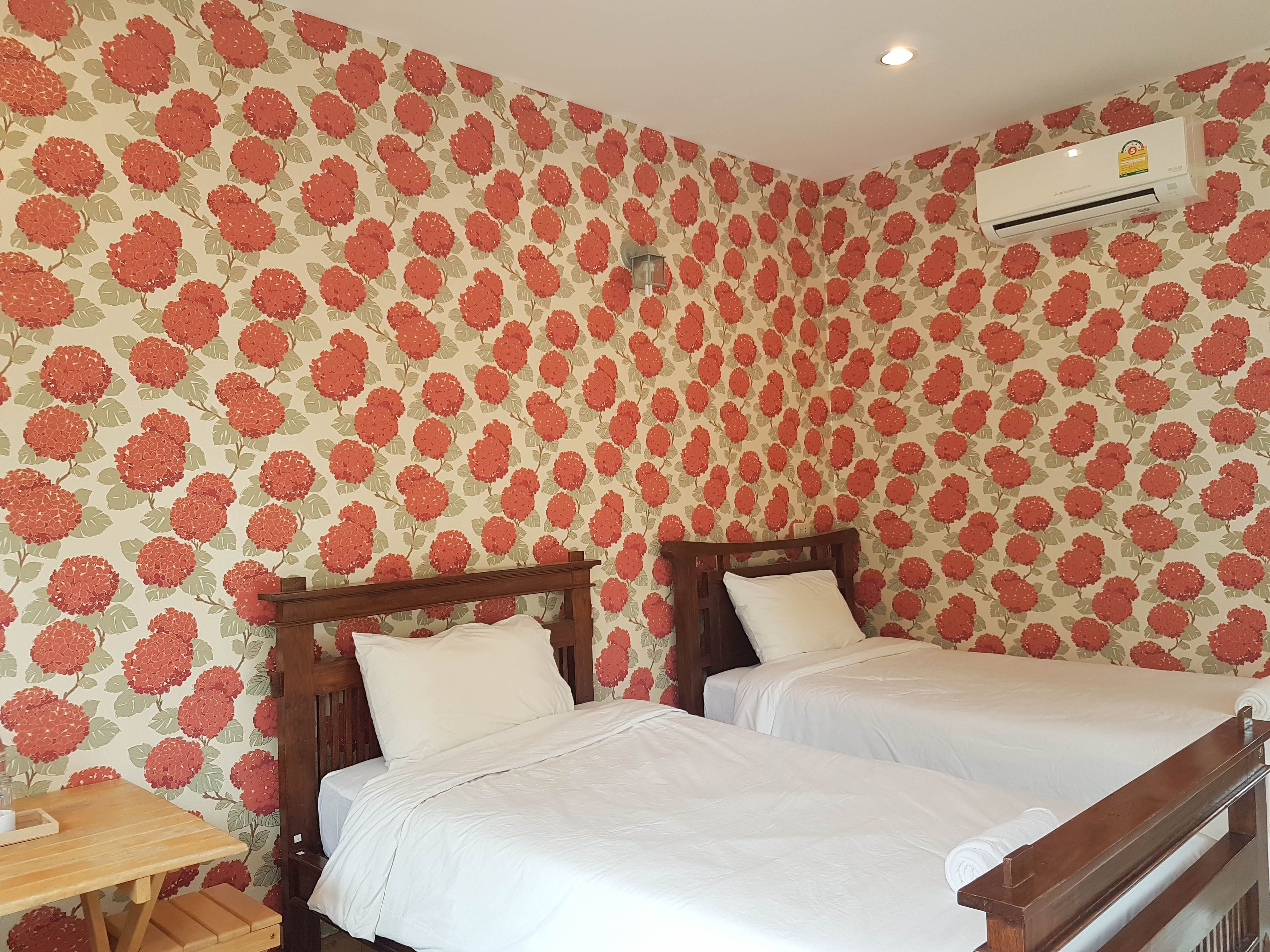 A room with two beds, a wooden desk, and a wall-mounted air conditioner.