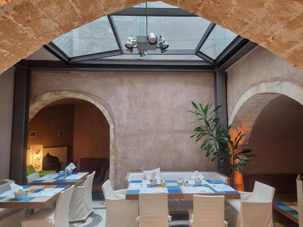 A dining area with a table set for four, under a glass ceiling with a chandelier.