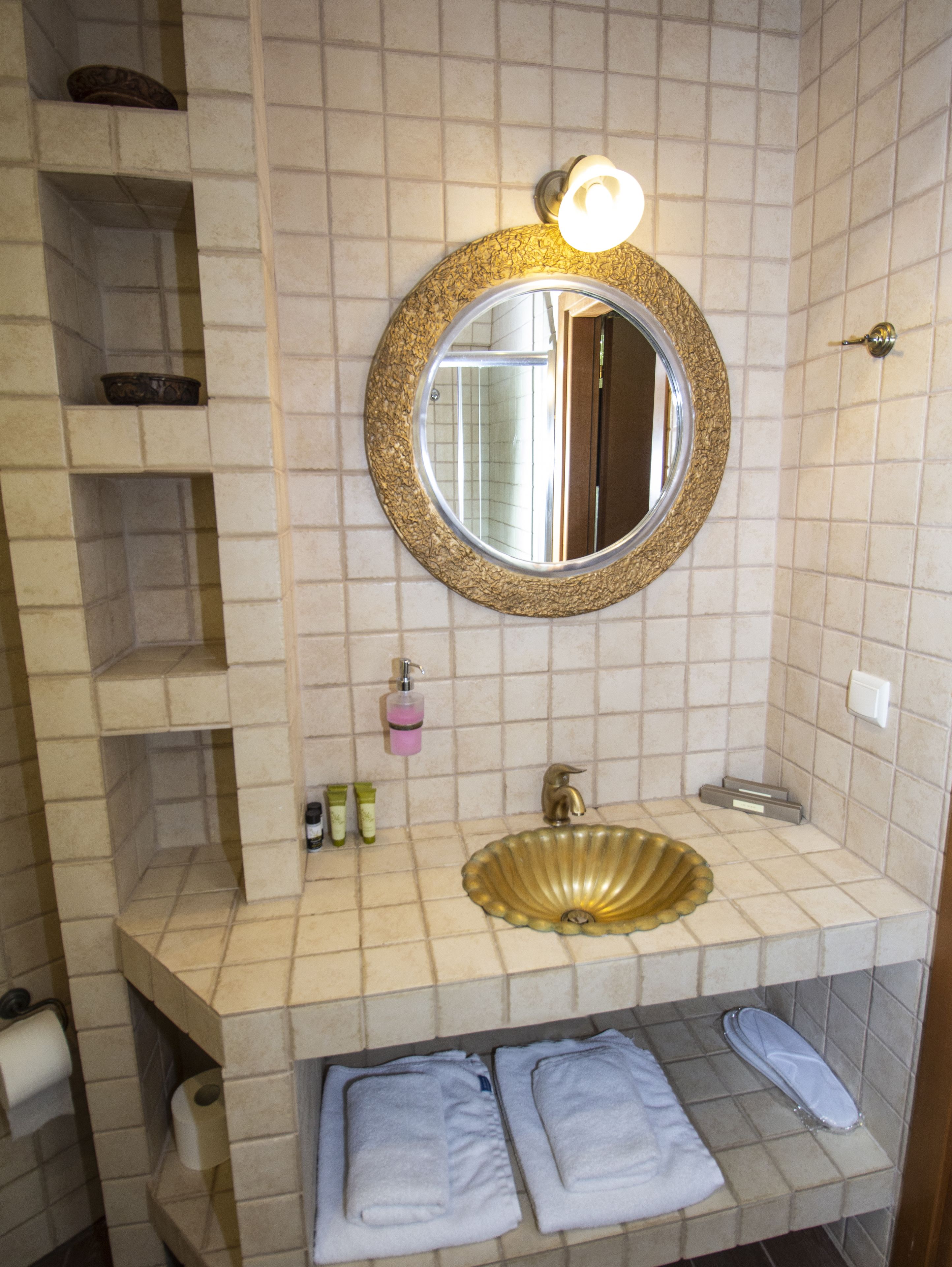 A bathroom with a round mirror, a gold sink, and a towel rack.