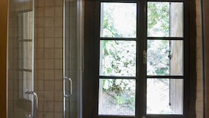 Un baño con cabina de ducha de vidrio, una ventana con vistas a la vegetación y paredes de azulejos.