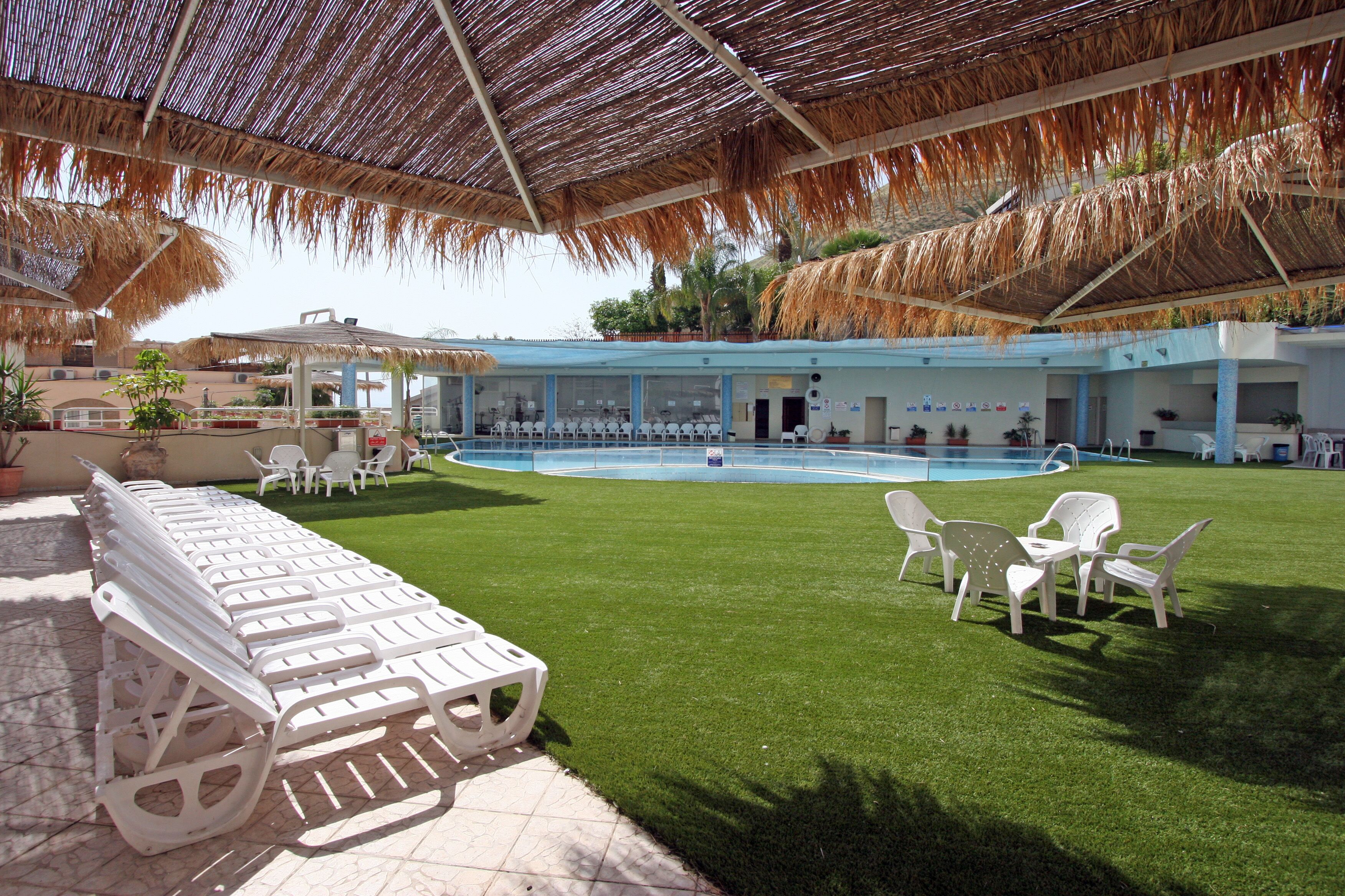 Un espace piscine doté de chaises longues et d’une structure à toit de chaume.