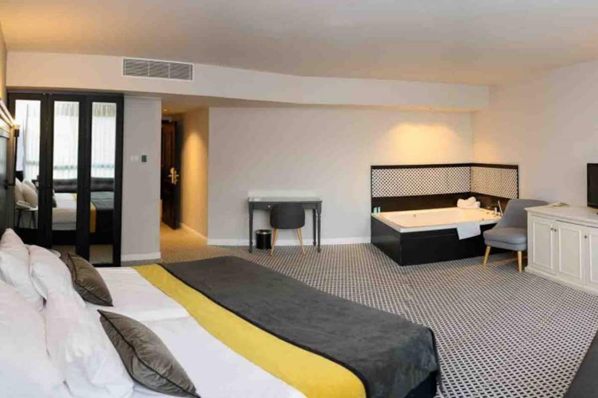 A hotel room with a large bed, a desk, a TV, and a bathroom with a bathtub.
