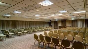 A conference room with rows of chairs, a stage, and a carpeted floor.