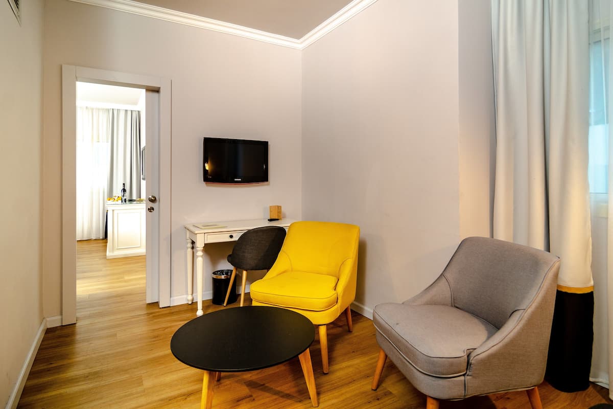 A modern hotel room with a wooden floor, a desk, a television, and two chairs.
