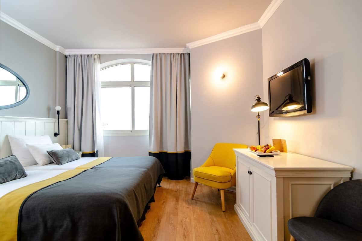 A hotel room with a bed, a desk with a lamp, a chair, and a TV mounted on the wall.
