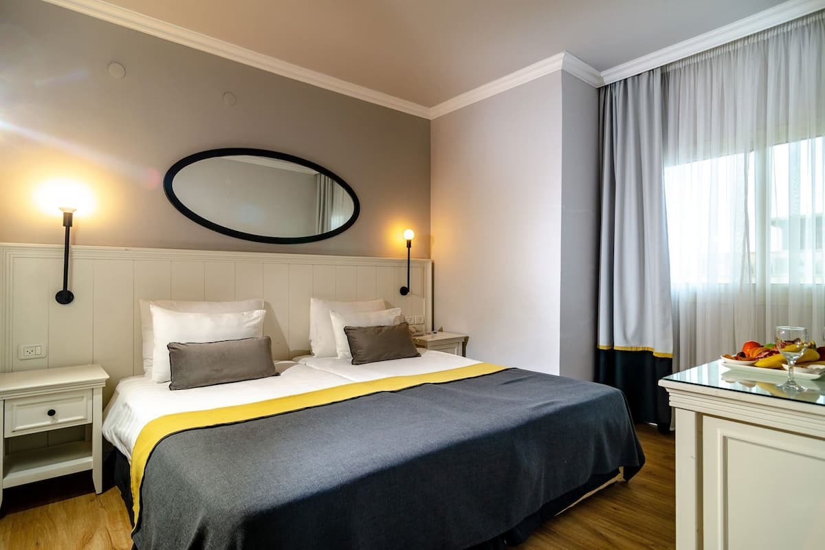 A hotel room with a bed, bedside tables, a mirror, a dresser, and a breakfast bar with fruit.