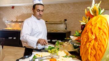 A buffet setup with a chef preparing food, a large carved pineapple centerpiece, and various dishes on display.