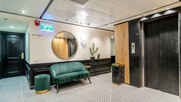 Un lobby moderno con un sofá verde, un espejo redondo, un cactus y un ascensor.
