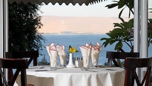 Une table dressée pour deux personnes, avec vue sur la mer et les collines.