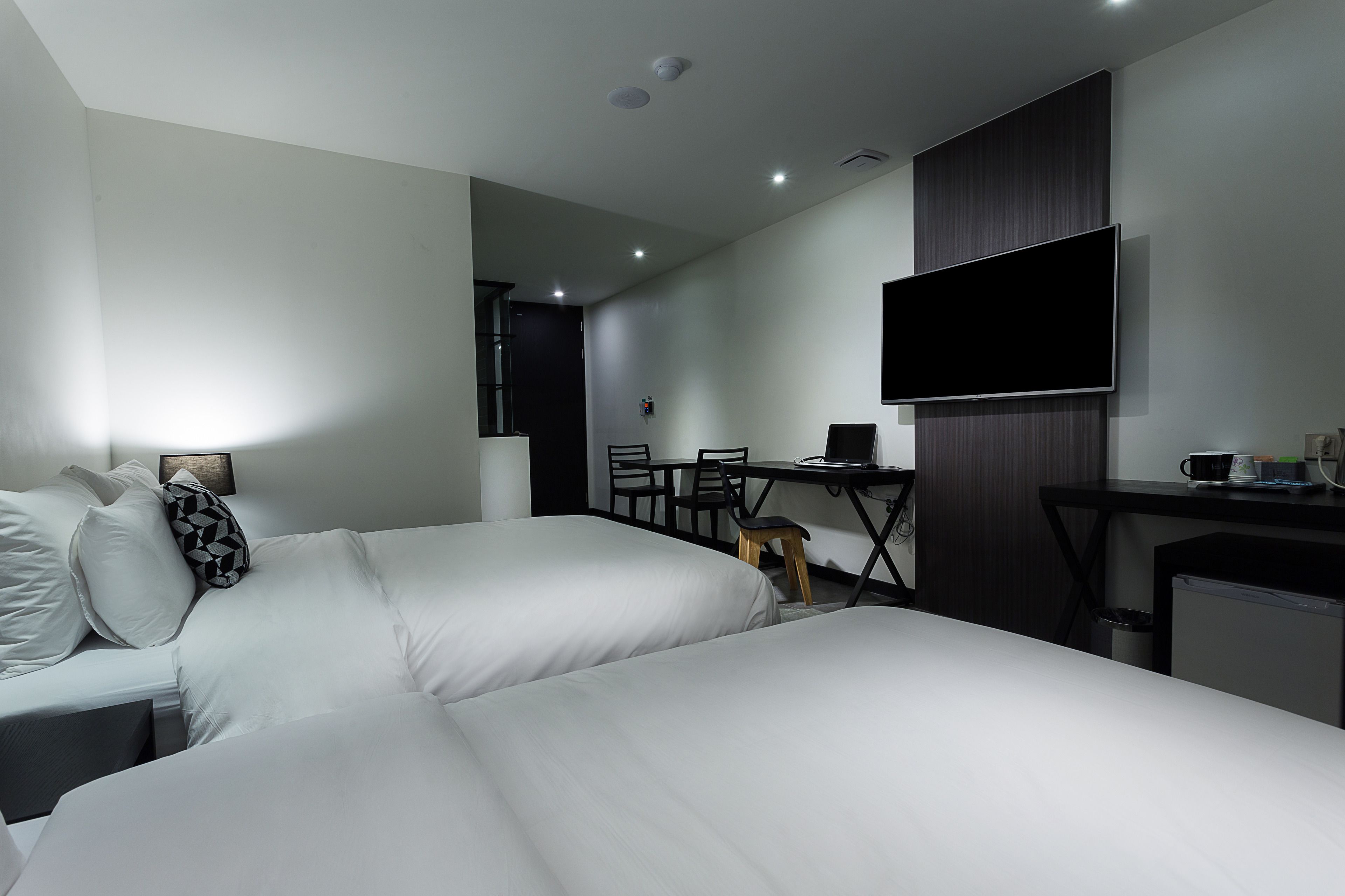 Una habitación de hotel moderna con dos camas, un escritorio, una silla, un televisor y una kitchenette pequeña.