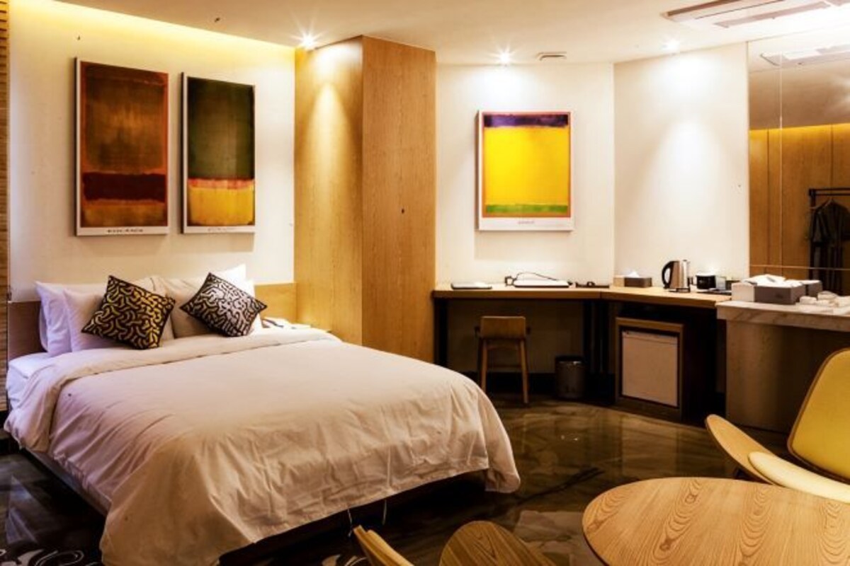 Une chambre d’hôtel avec un lit, un bureau, une chaise et des œuvres d’art accrochées aux murs.