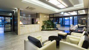A modern hotel lobby with a reception desk, seating area, and large windows offering views of the outdoors. - Hotel Sienna (Paju)