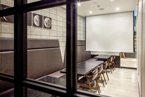 A modern restaurant with a long counter, cushioned seating, and a large projection screen.