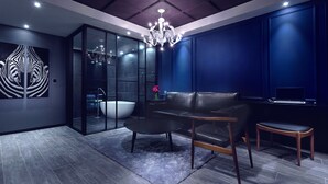 A modern interior with a dark blue wall, a black leather sofa, a wooden bench, and a glass partition leading to a bathroom. - Hotel Sienna (Paju)