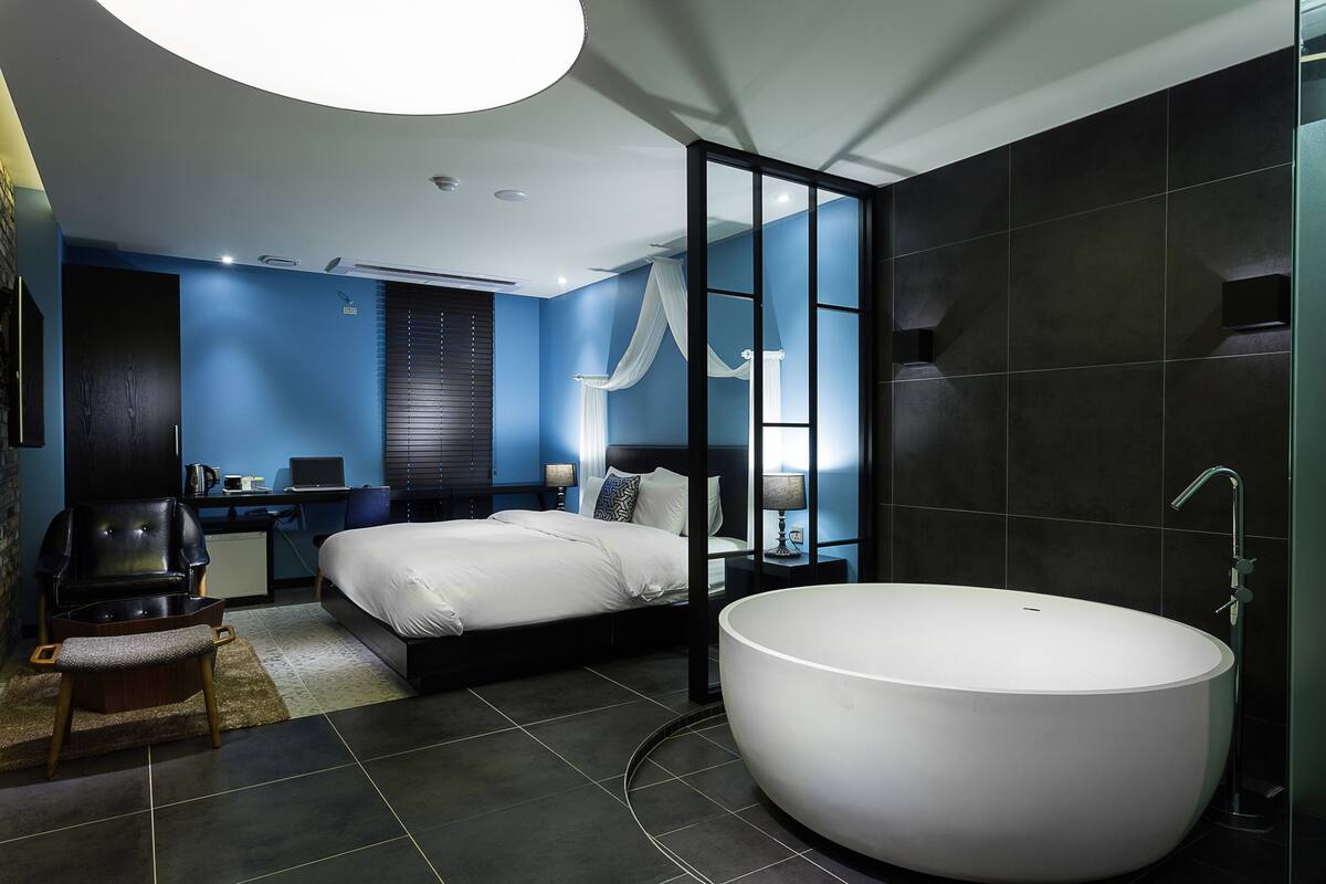 A modern bedroom with a large bed, a sitting area, and a freestanding bathtub.