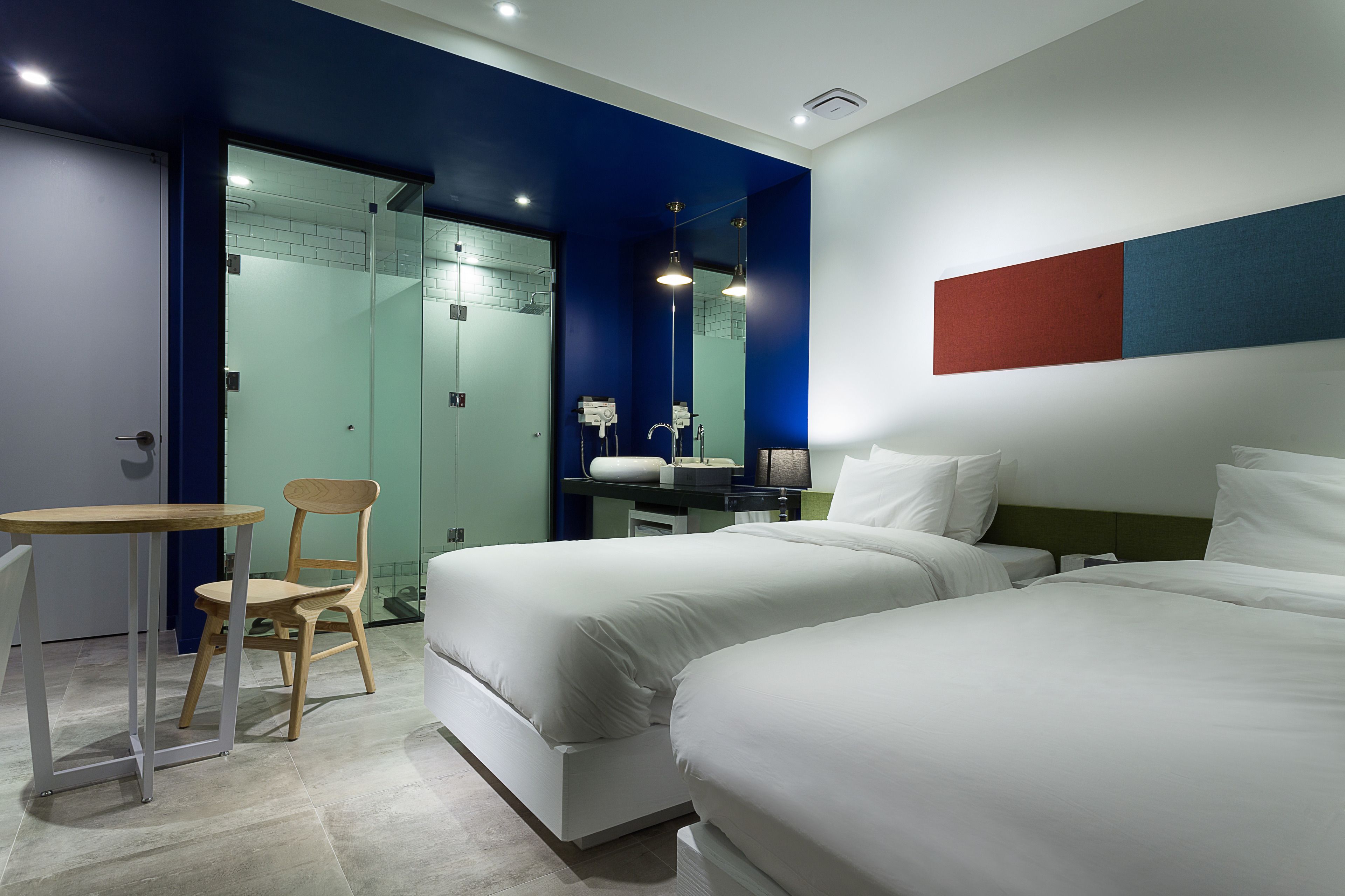A modern hotel room with two beds, a desk, and a chair.