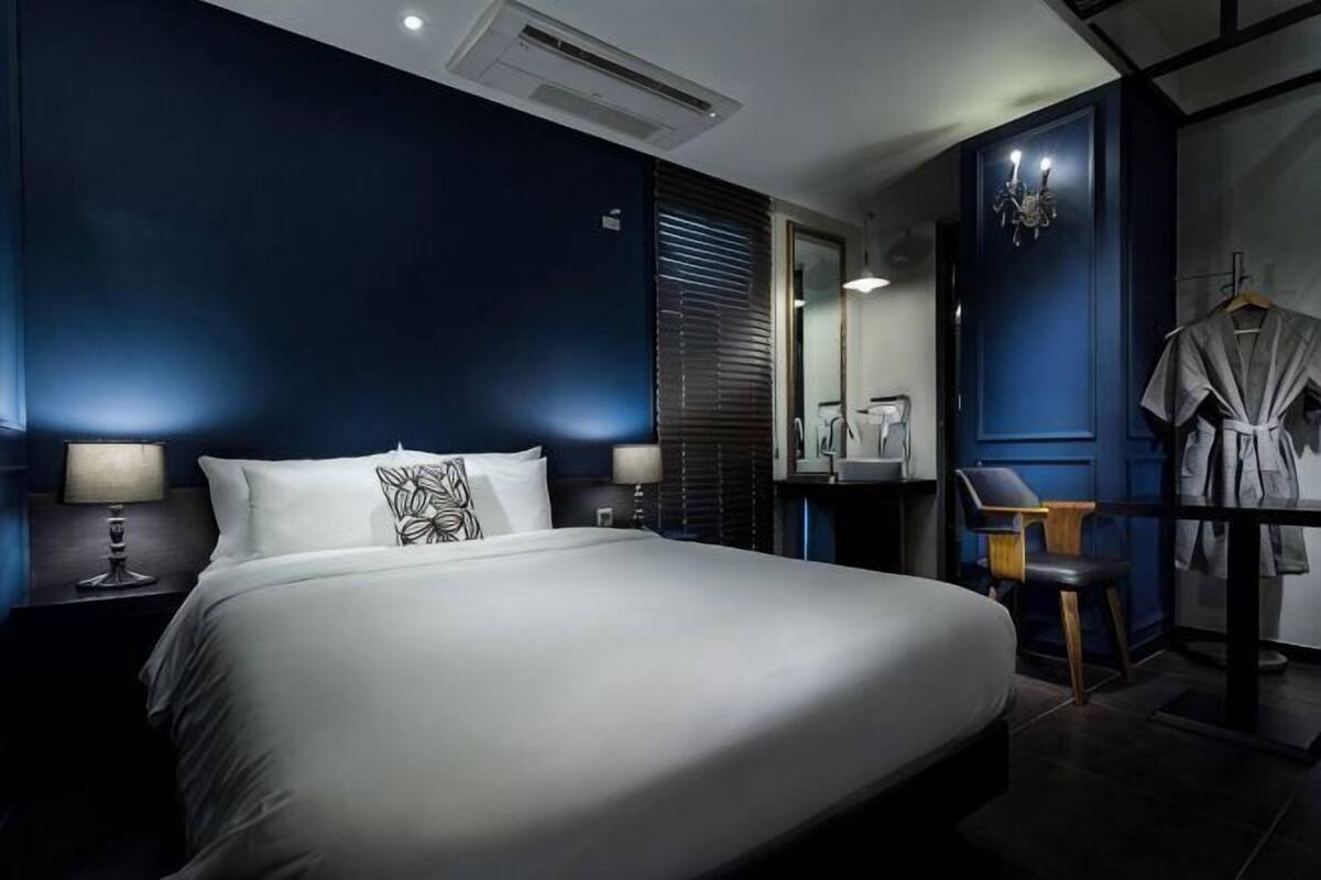 A hotel room with a large bed, bedside lamps, a mirror, a robe, and a desk with a chair.