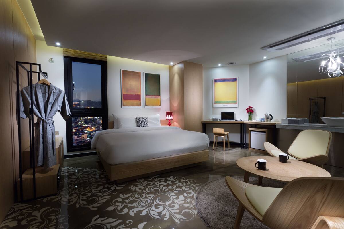 A modern hotel room with a large bed, a desk, a chair, and a view of the city at night.