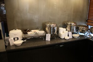 A buffet setup with various food containers, bowls, and utensils on a counter.
