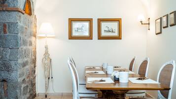 Un comedor con pared de piedra, una mesa con sillas blancas, cuadros en la pared y una lámpara de pie.