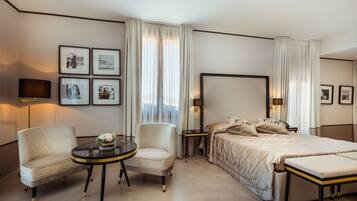 A hotel room with a large bed, two armchairs, a small table with a vase, and framed pictures on the wall.