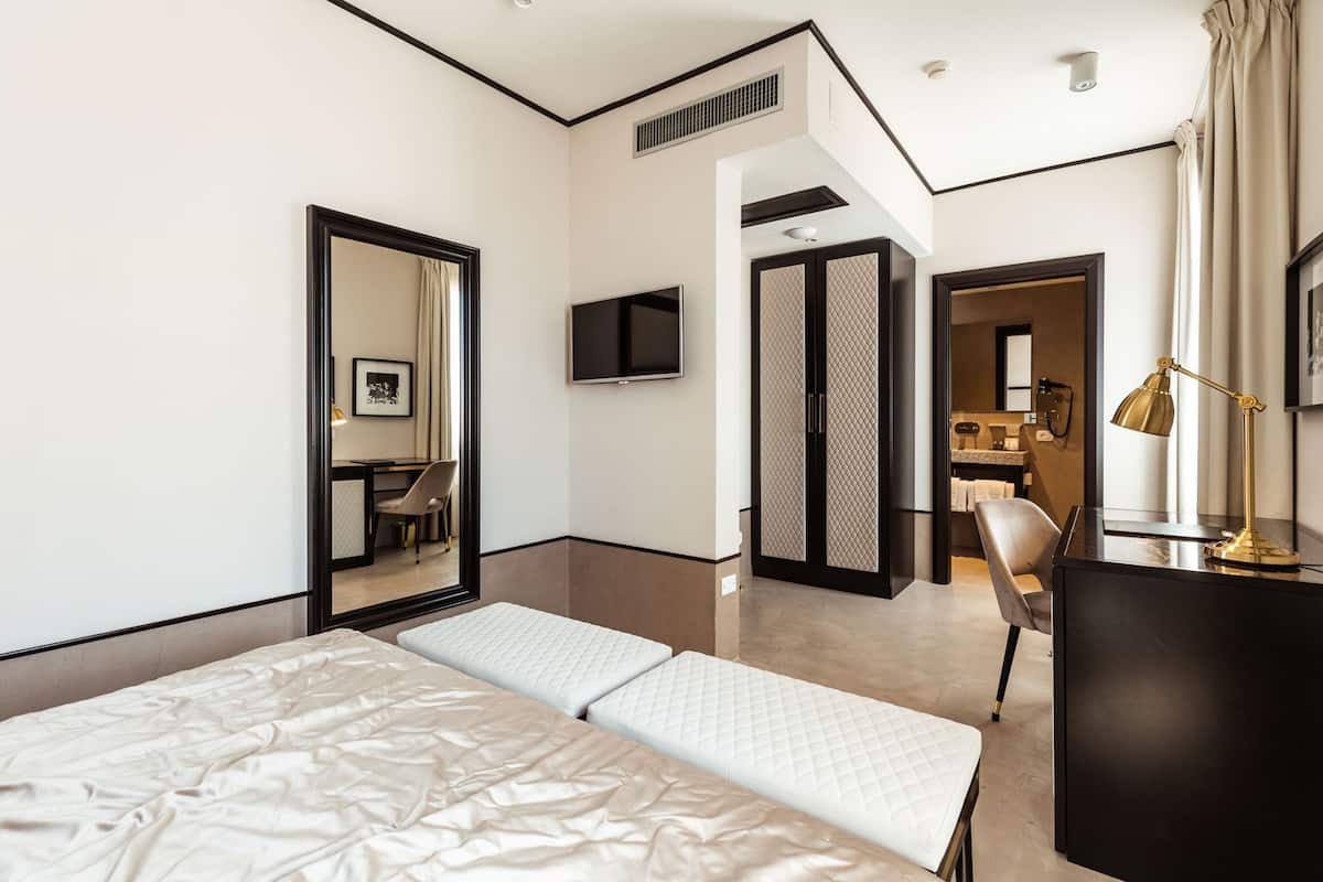 A modern hotel room with a bed, a desk, a chair, a TV, and a desk lamp.