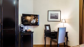 Ein Hotelzimmer mit Fernseher, Schreibtisch mit Stuhl, gerahmtem Bild an der Wand und Lampe.