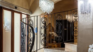 A grand staircase with ornate black railings, a chandelier, and white orchids at the base. - La Locanda del Conte Mameli (Olbia)