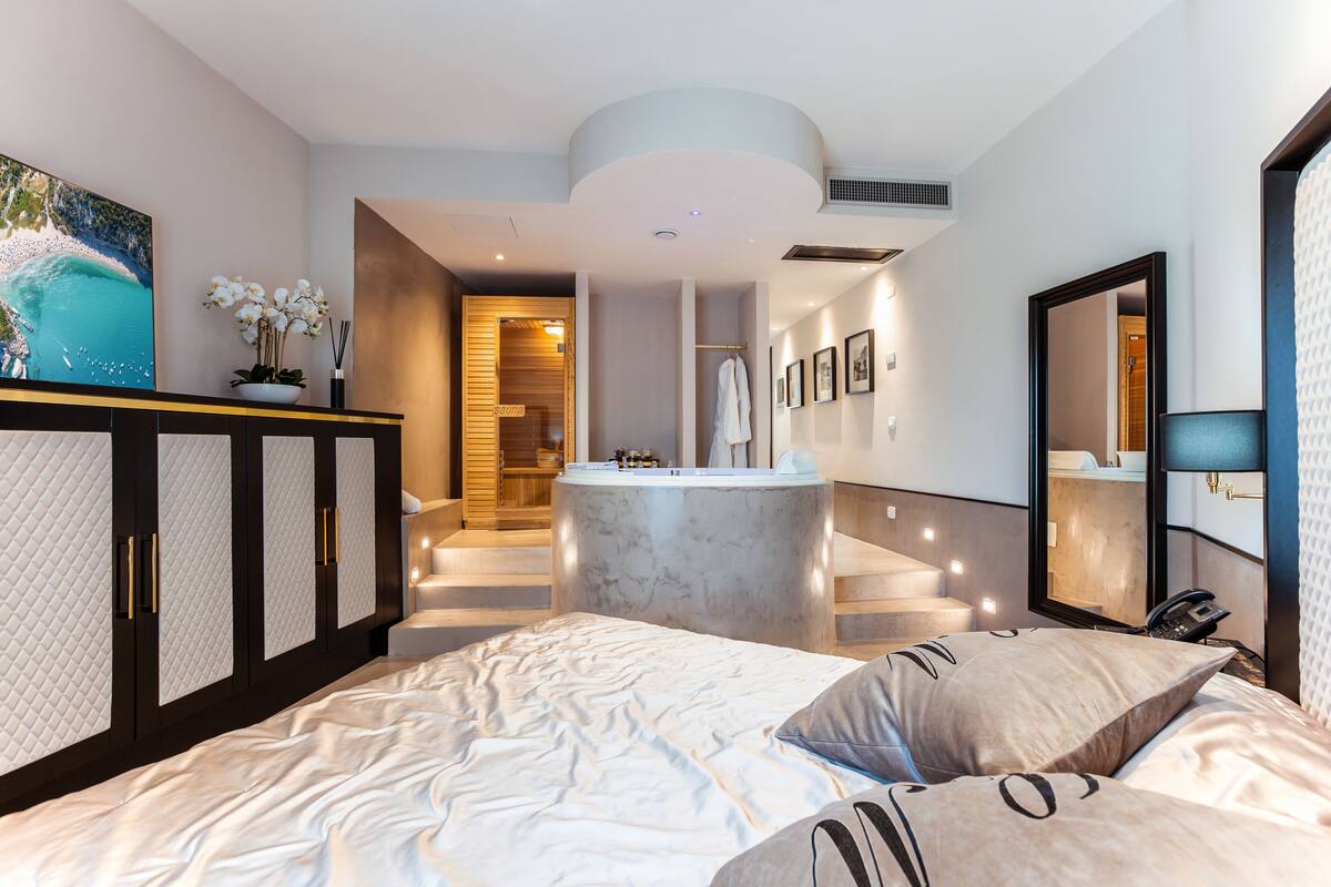 A modern hotel room with a large bed, a marble bathroom, and a view of the sea.