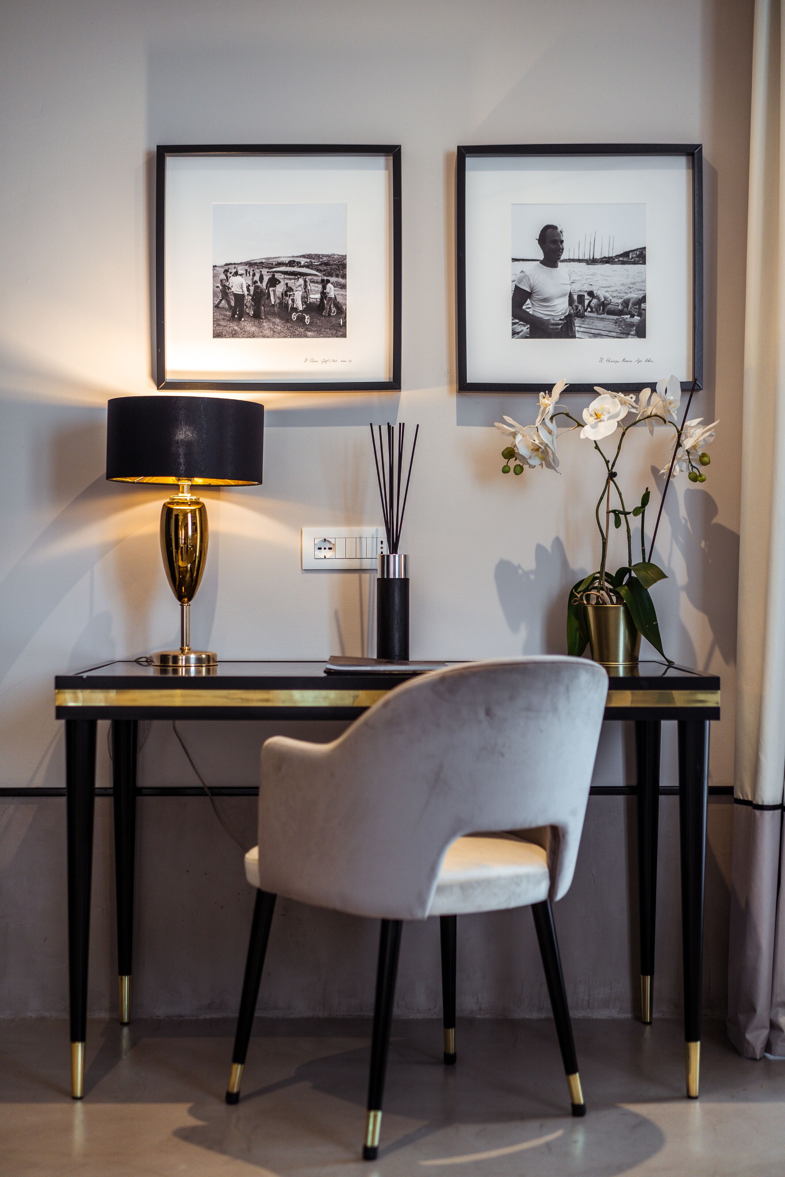 Una habitación moderna con un escritorio, fotografías enmarcadas en la pared, una lámpara, una silla y una planta de orquídea.
