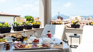 A breakfast spread on a terrace with a city view, including various cheeses, meats, and bread. - La Locanda del Conte Mameli (Olbia)
