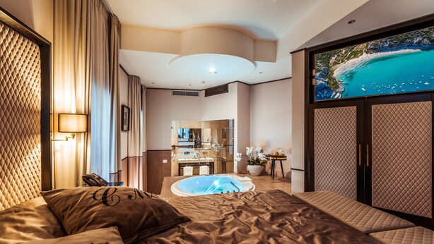 A luxurious hotel room with a large bed, a jacuzzi, a view of a beach, and a modern bathroom. - La Locanda del Conte Mameli (Olbia)