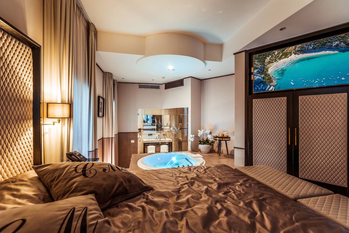 A luxurious hotel room with a large bed, a jacuzzi, a view of a beach, and a modern bathroom.