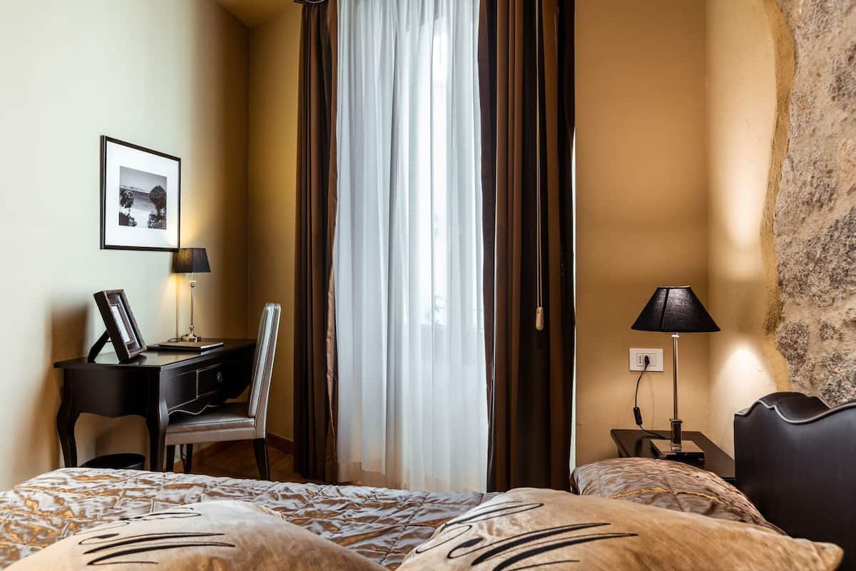 A hotel room with a bed, a desk, a chair, a lamp, and a picture on the wall.