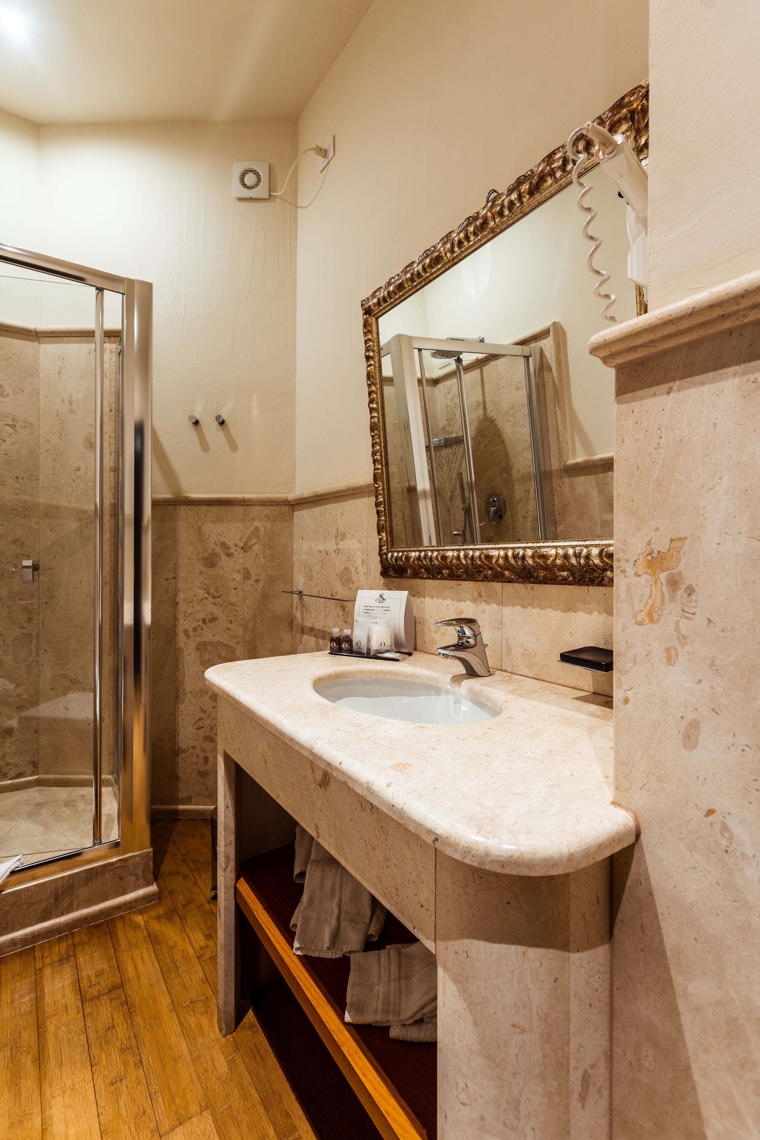 A bathroom with a glass shower enclosure, a marble sink, and a large mirror with a gold frame.