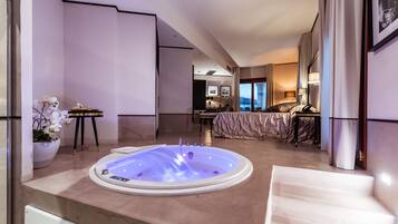 A modern hotel room with a large bathtub, a bed, and a dining area.