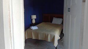 A small, single-bed room with a wooden headboard, a bedside lamp, and a door with a number sign.