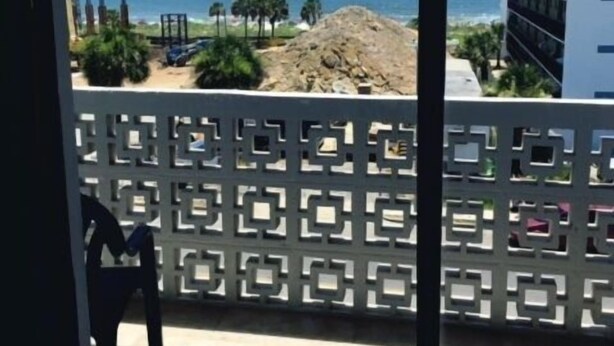 A view from a room with a window overlooking a beach, a building, and a decorative fence.