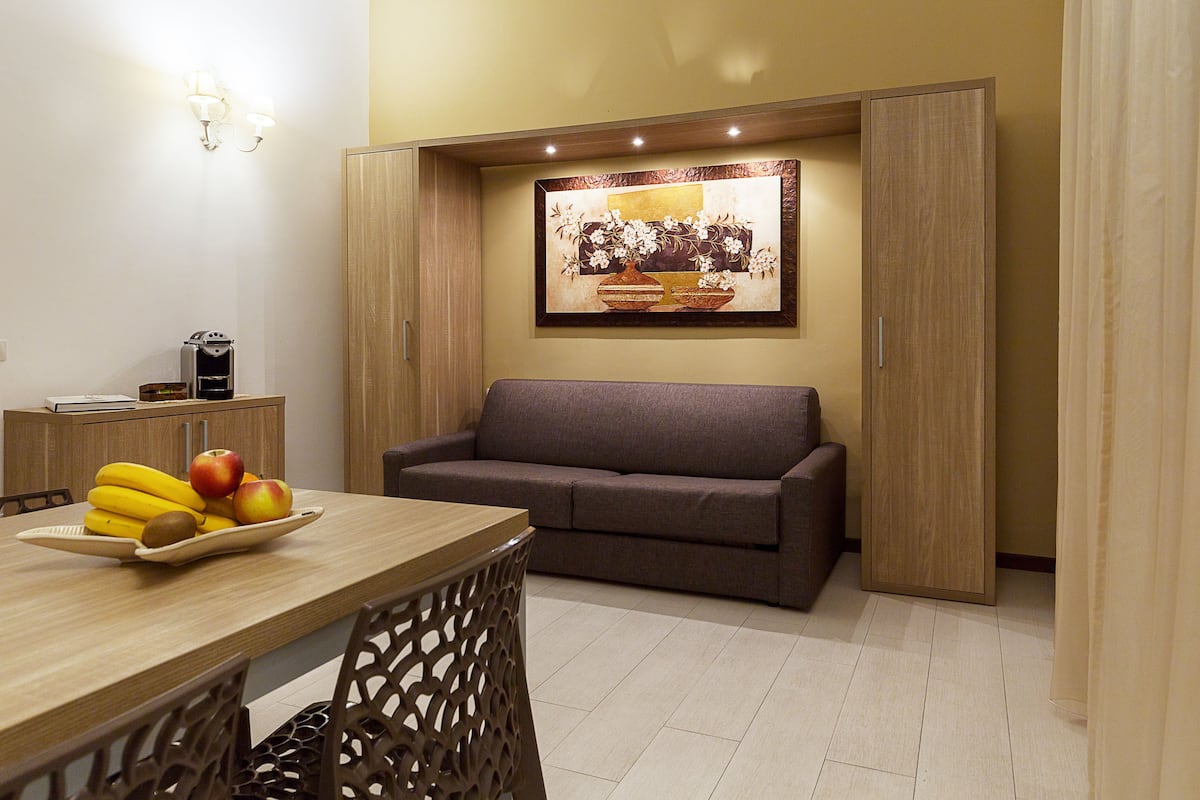 A modern living room with a sofa, a dining table with fruit, and a coffee machine.