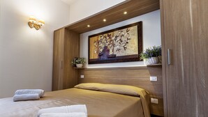 A hotel room with a bed, two towels, a wall-mounted painting, and a shelf with plants. - Le Residenze del Centro (Olbia)