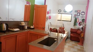 A compact kitchen with a sink, a stove, and a dining area with a red sofa. - Stylus Hotel (Iquitos)