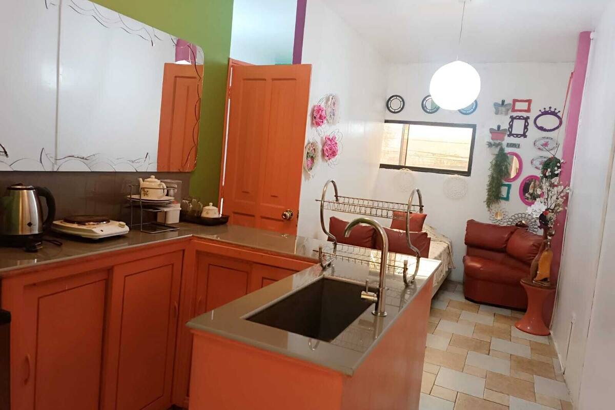 A compact kitchen with a sink, a stove, and a dining area with a red sofa.