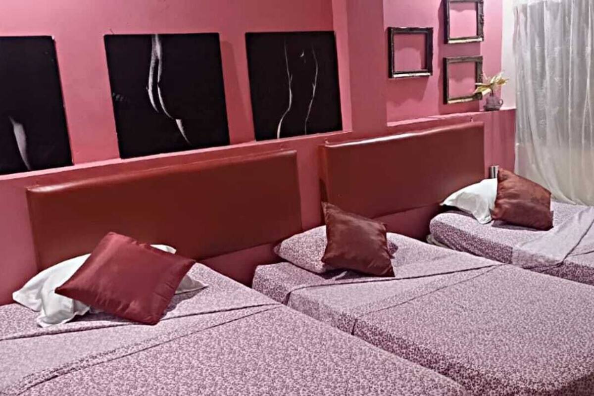 A room with two beds, each with a pink bedspread and pillows, against a pink wall with abstract art.